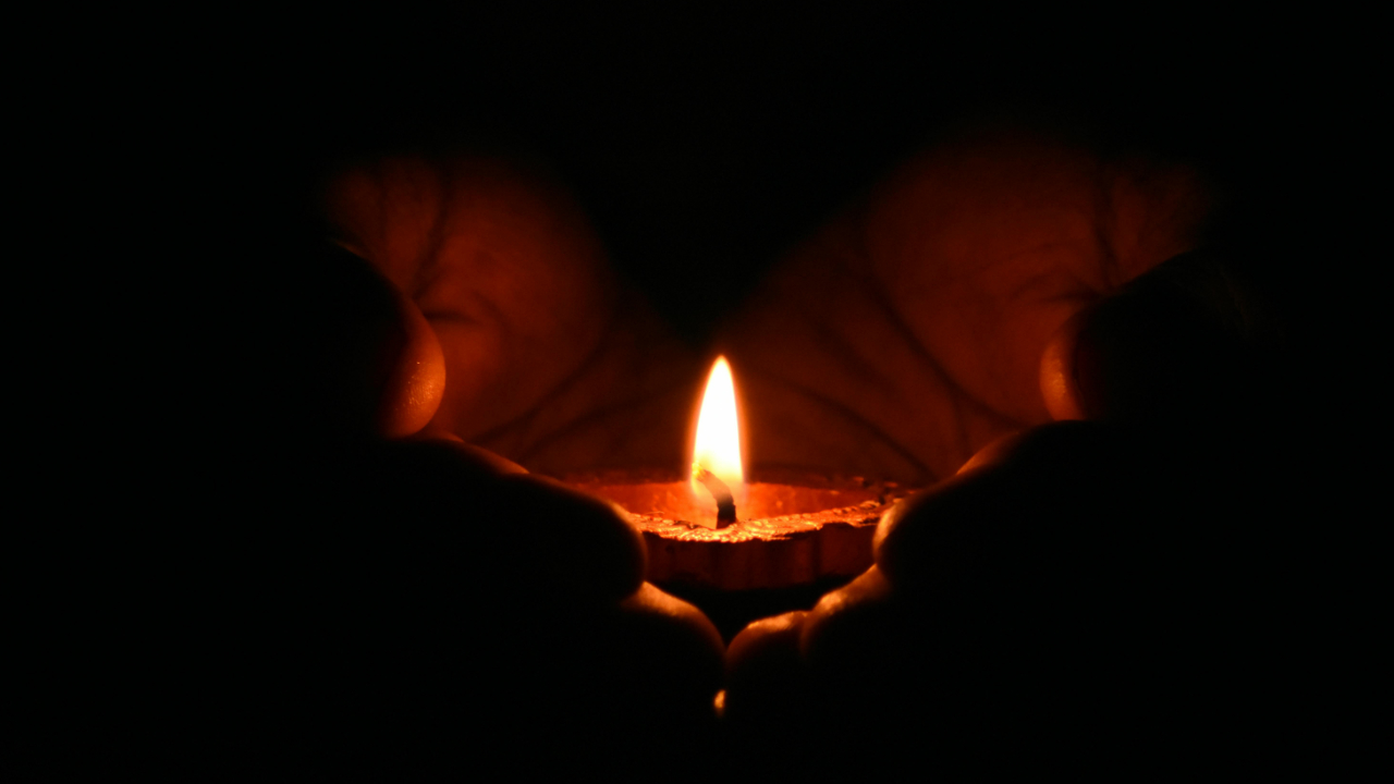 two hands cupping a lit candle