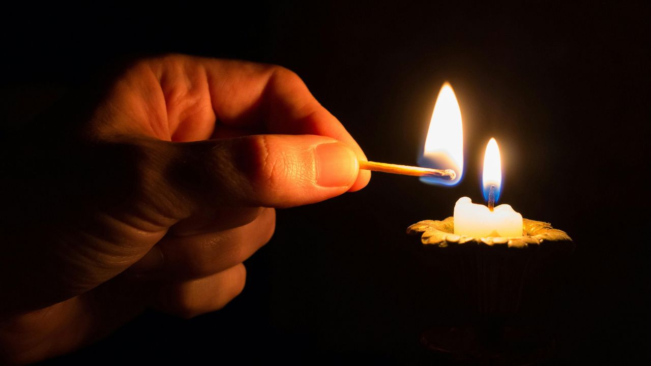 the hand of a man lighting a candle in the darkness